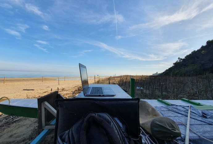 Un computer portatile su un tavolo in spiaggia, con uno zaino e il mare sullo sfondo