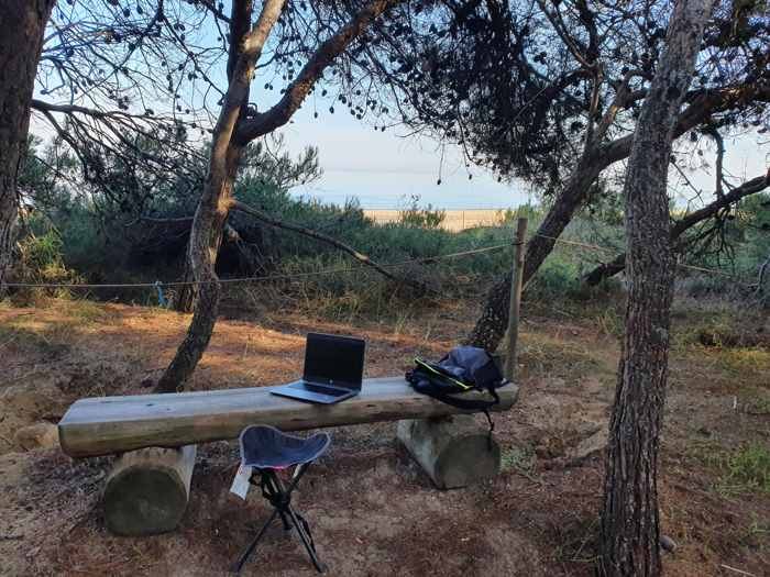 Un portatile appoggiato su una panca di legno nella pineta
